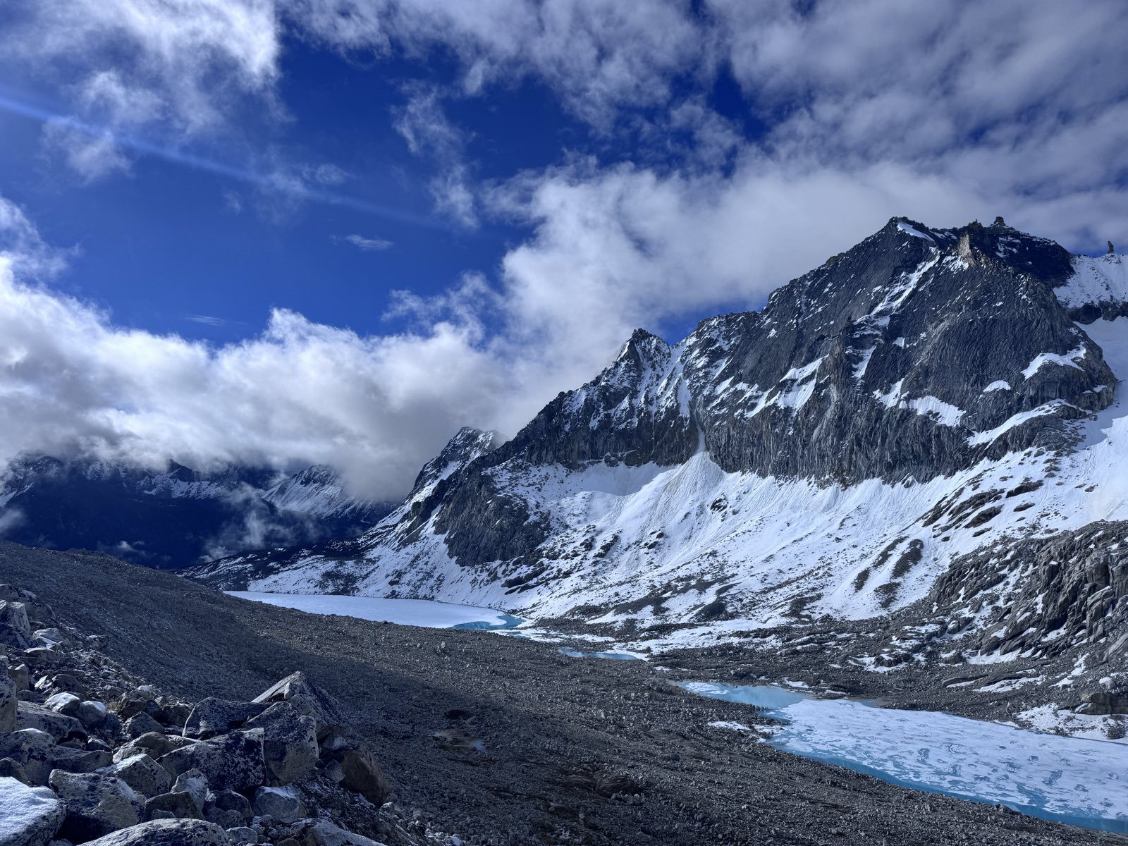 A snow-covered peak above a glacial valley of meltwater pools and moraine